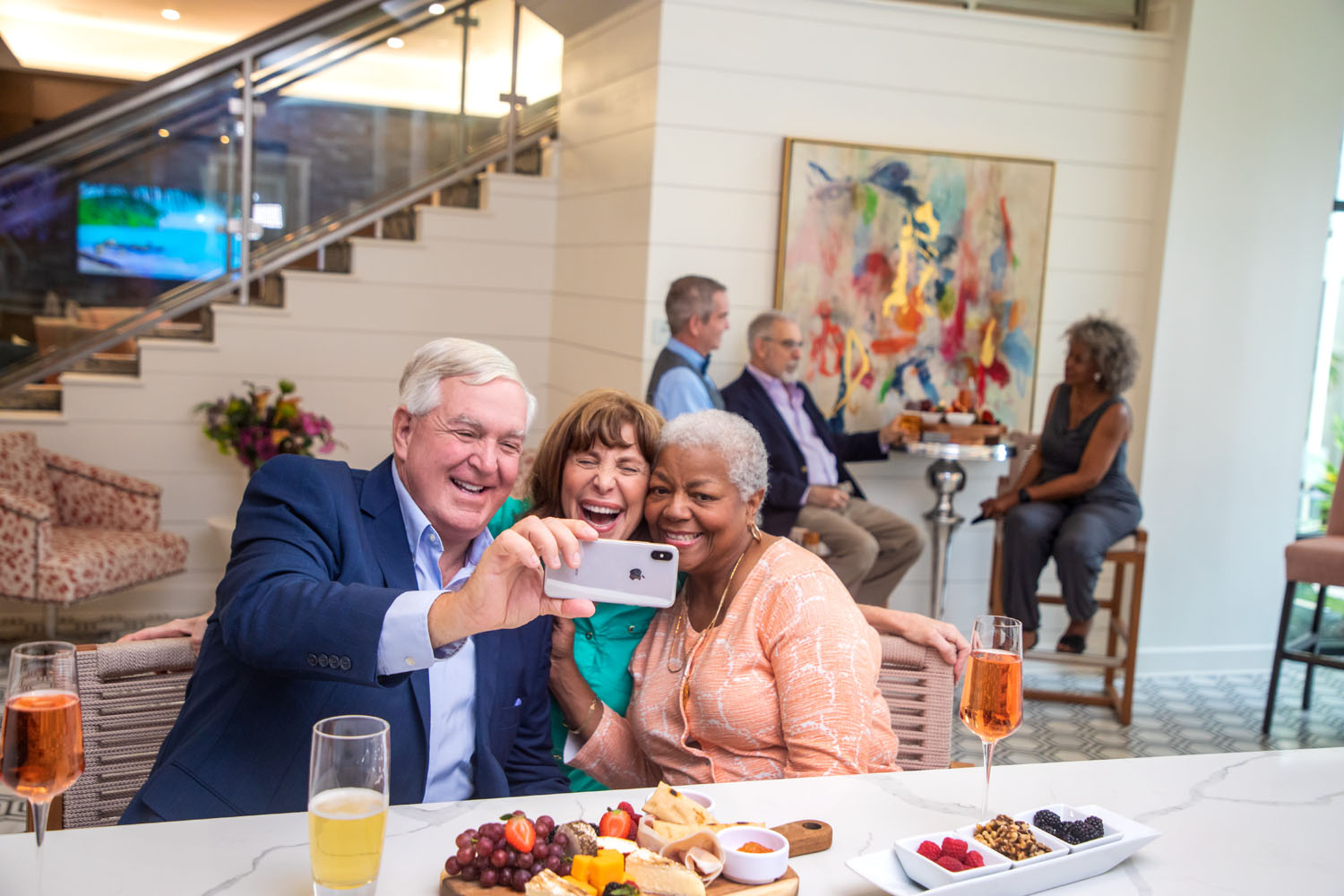 Senior residents taking a selfie on an iphone at the bar area with drinks and snacks